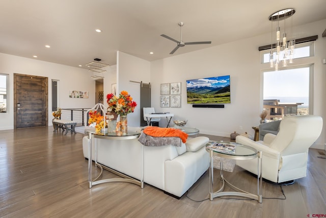 living room featuring ceiling fan with notable chandelier, a barn door, and hardwood / wood-style flooring