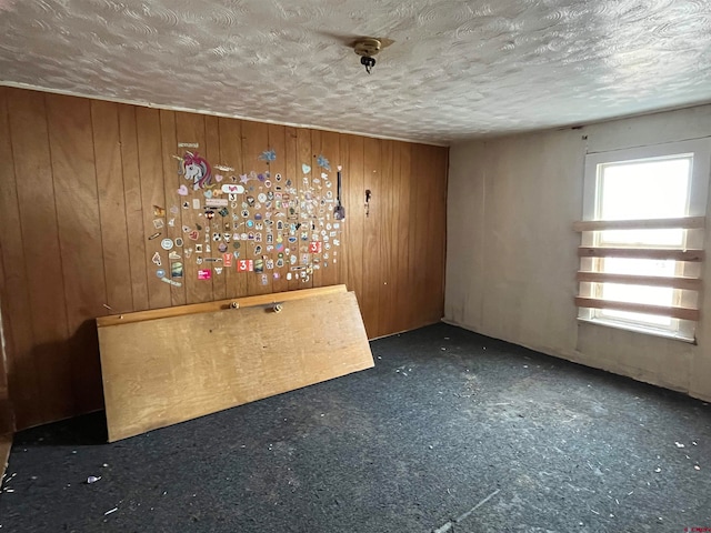 unfurnished room featuring dark colored carpet, wooden walls, and a textured ceiling