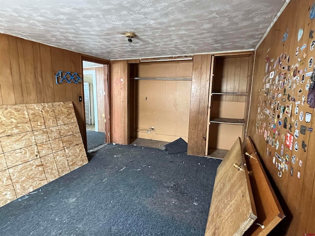 unfurnished bedroom with wood walls, dark colored carpet, and a textured ceiling