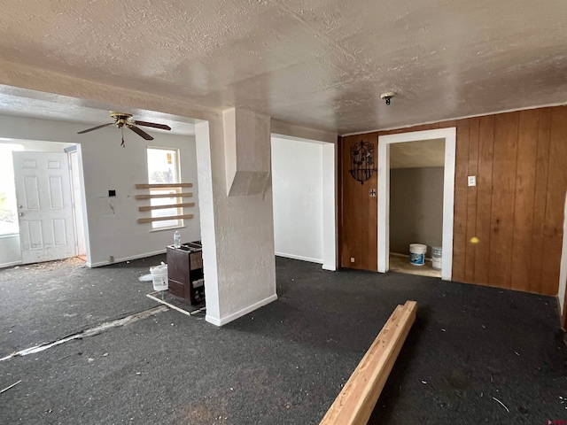 unfurnished living room featuring wood walls, a textured ceiling, and ceiling fan