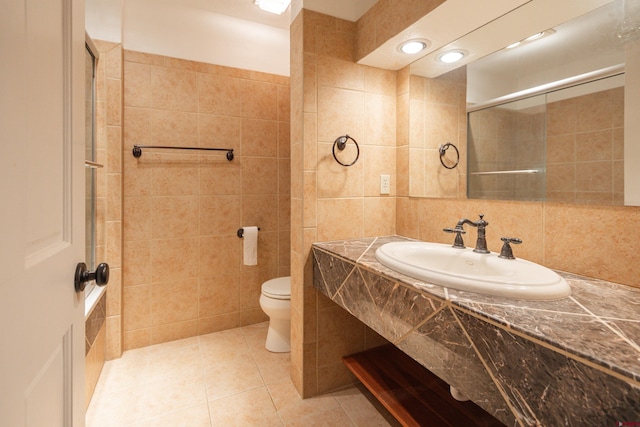 bathroom with a shower with shower door, tile patterned floors, sink, and tile walls