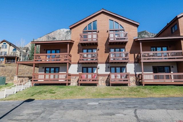 back of property featuring a deck with mountain view, a lawn, and a balcony