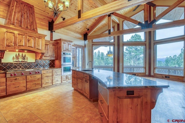 kitchen with stainless steel appliances, a large island with sink, beam ceiling, dark stone countertops, and wooden ceiling