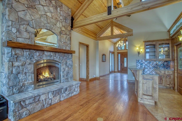 unfurnished living room featuring a fireplace, high vaulted ceiling, light hardwood / wood-style floors, beamed ceiling, and wooden ceiling