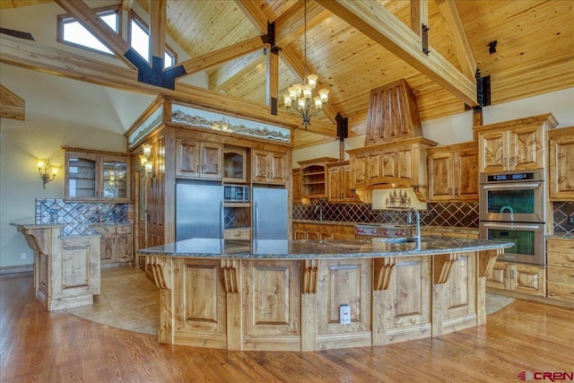 kitchen with dark stone counters, high vaulted ceiling, a large island with sink, and appliances with stainless steel finishes