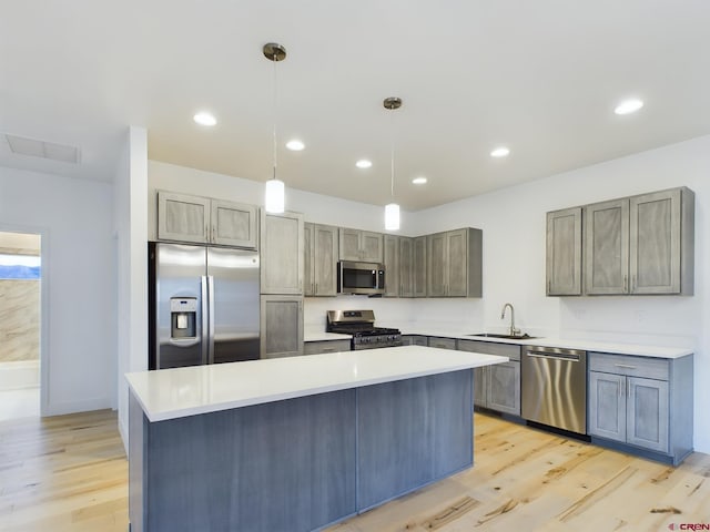 kitchen featuring a kitchen island, pendant lighting, sink, light wood-type flooring, and appliances with stainless steel finishes