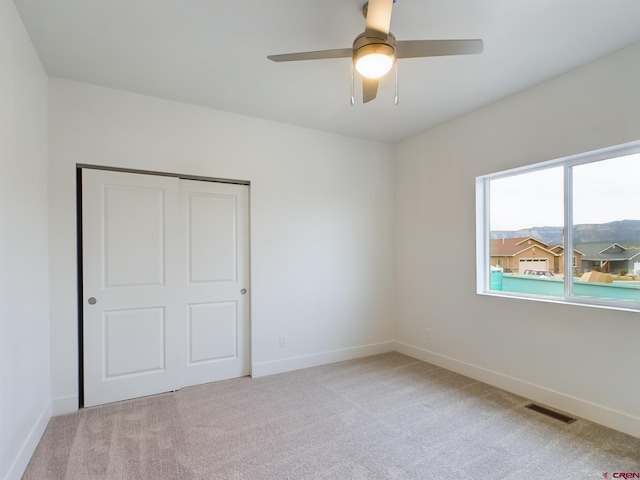 unfurnished bedroom with ceiling fan, a closet, and light carpet