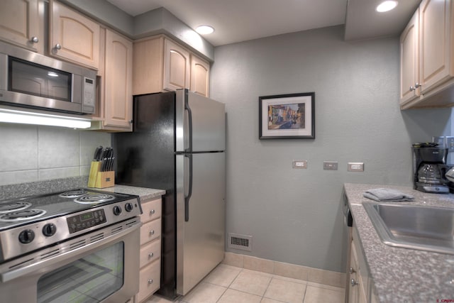 kitchen featuring light brown cabinetry, decorative backsplash, light tile patterned floors, and stainless steel appliances