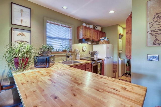 kitchen featuring sink, kitchen peninsula, wood counters, stainless steel stove, and white refrigerator