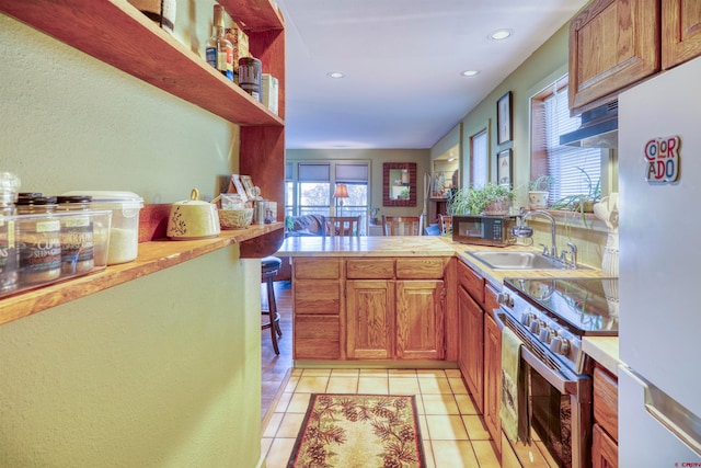 kitchen with white refrigerator, kitchen peninsula, sink, light tile patterned floors, and high end stainless steel range