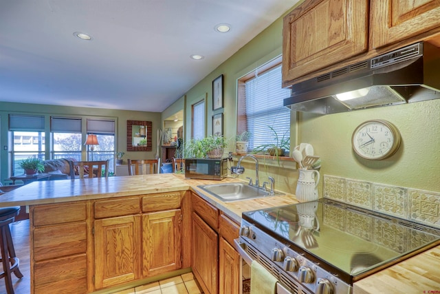 kitchen with light tile patterned flooring, stainless steel stove, wood counters, sink, and kitchen peninsula