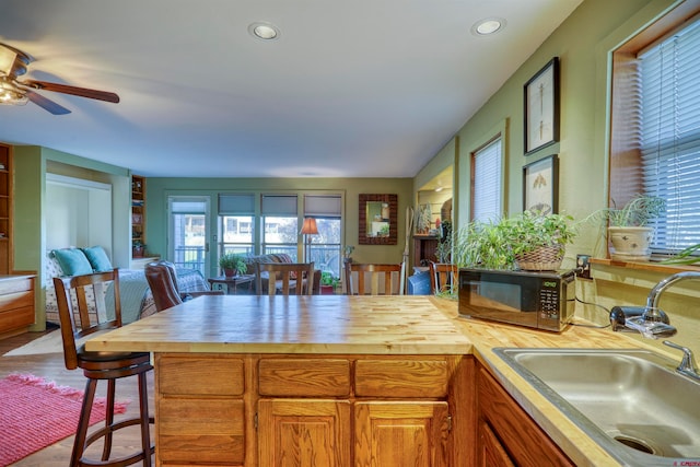 kitchen with hardwood / wood-style flooring, sink, a breakfast bar, wooden counters, and ceiling fan