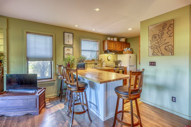 kitchen with sink, a breakfast bar, wooden counters, white fridge, and light wood-type flooring