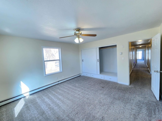 unfurnished bedroom with multiple windows, dark carpet, baseboard heating, and ceiling fan