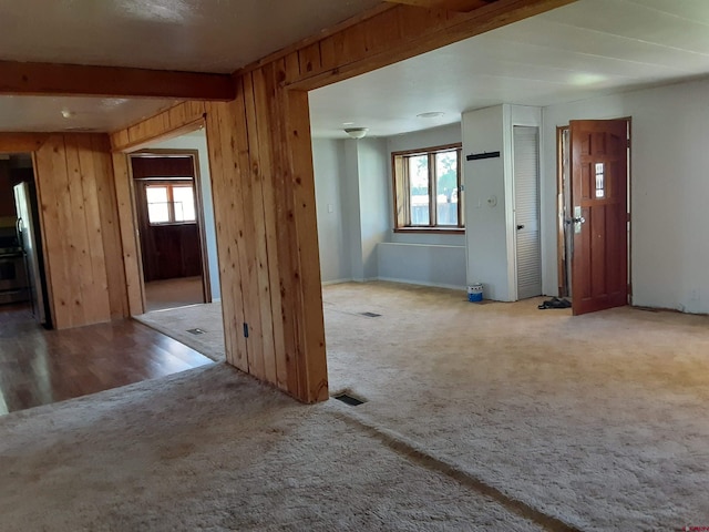 interior space featuring wood walls, beam ceiling, a healthy amount of sunlight, and light hardwood / wood-style flooring