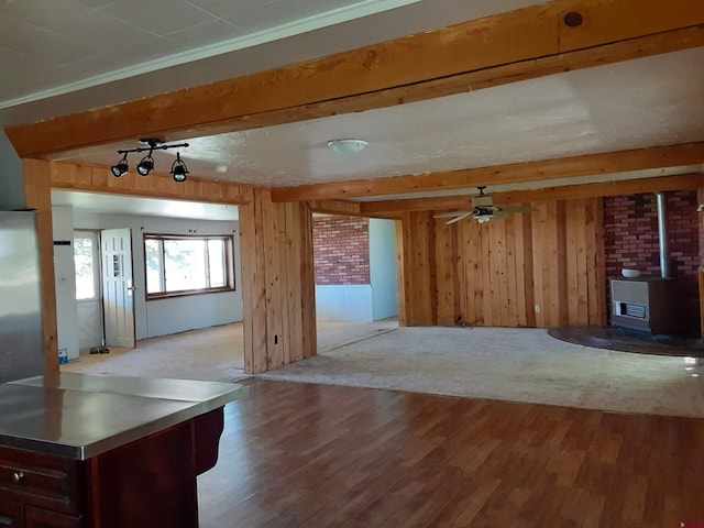 unfurnished living room featuring a wood stove, beam ceiling, wooden walls, ceiling fan, and light hardwood / wood-style flooring