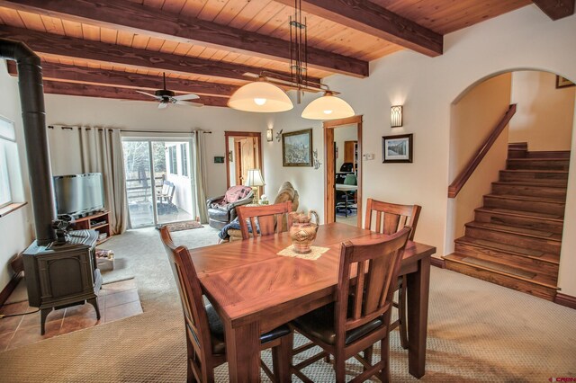 dining room with light colored carpet, wood ceiling, a wood stove, beamed ceiling, and ceiling fan