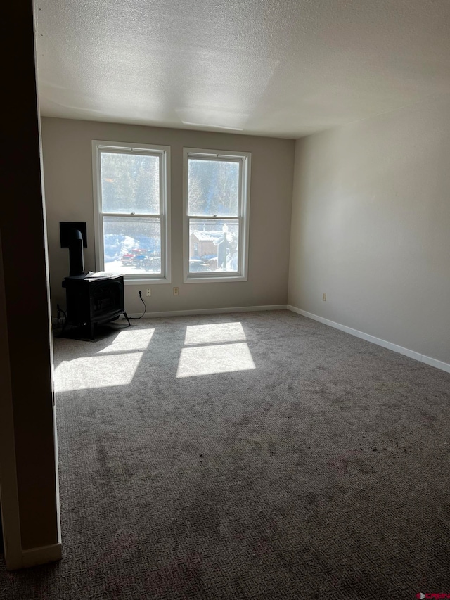 carpeted empty room featuring a wood stove and a textured ceiling