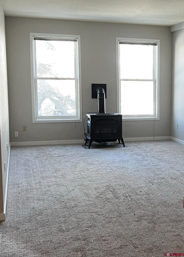 unfurnished room featuring light colored carpet and a wood stove