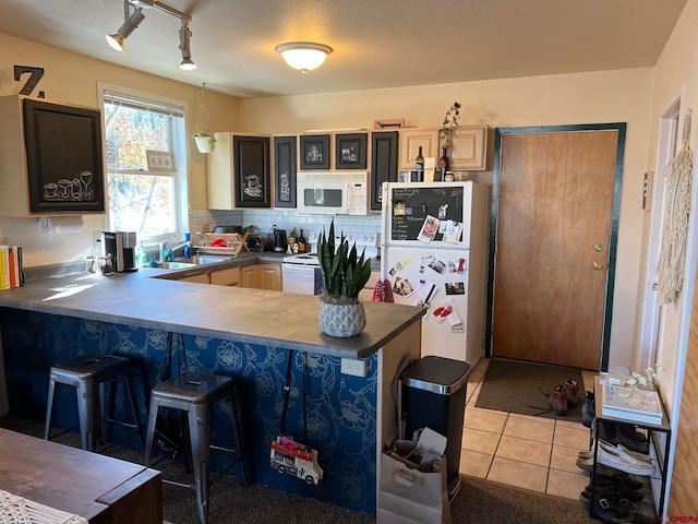 kitchen featuring light tile patterned flooring, sink, a breakfast bar, kitchen peninsula, and white appliances