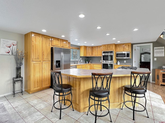 kitchen with sink, light tile patterned floors, a kitchen breakfast bar, a kitchen island, and appliances with stainless steel finishes