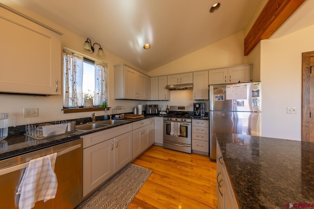 kitchen with dark stone countertops, stainless steel appliances, lofted ceiling, and light hardwood / wood-style floors