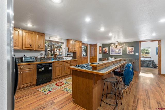 kitchen featuring light wood-type flooring, black dishwasher, a kitchen island, and a breakfast bar area