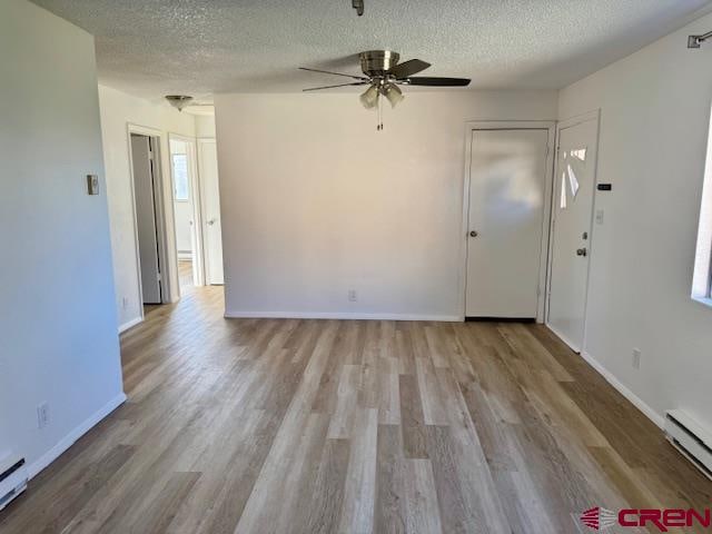 spare room featuring baseboard heating, ceiling fan, light hardwood / wood-style flooring, and a textured ceiling