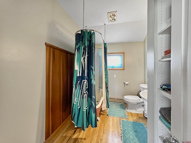 bathroom featuring shower / bath combo with shower curtain, toilet, wood-type flooring, and a baseboard heating unit