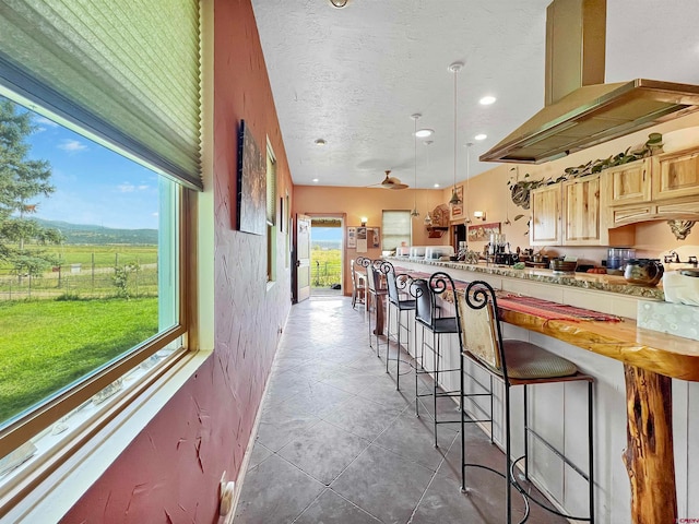 kitchen featuring pendant lighting, a kitchen breakfast bar, ceiling fan, dark tile patterned floors, and island range hood