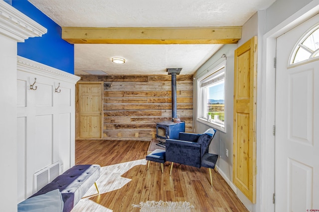 sitting room featuring a textured ceiling, beam ceiling, light hardwood / wood-style floors, a wood stove, and wood walls