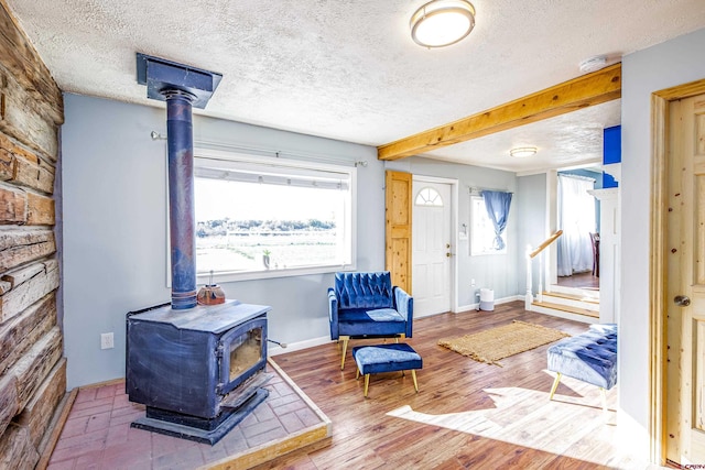 living area with beamed ceiling, hardwood / wood-style floors, a textured ceiling, and a wood stove