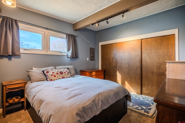 carpeted bedroom with beamed ceiling, a closet, and track lighting