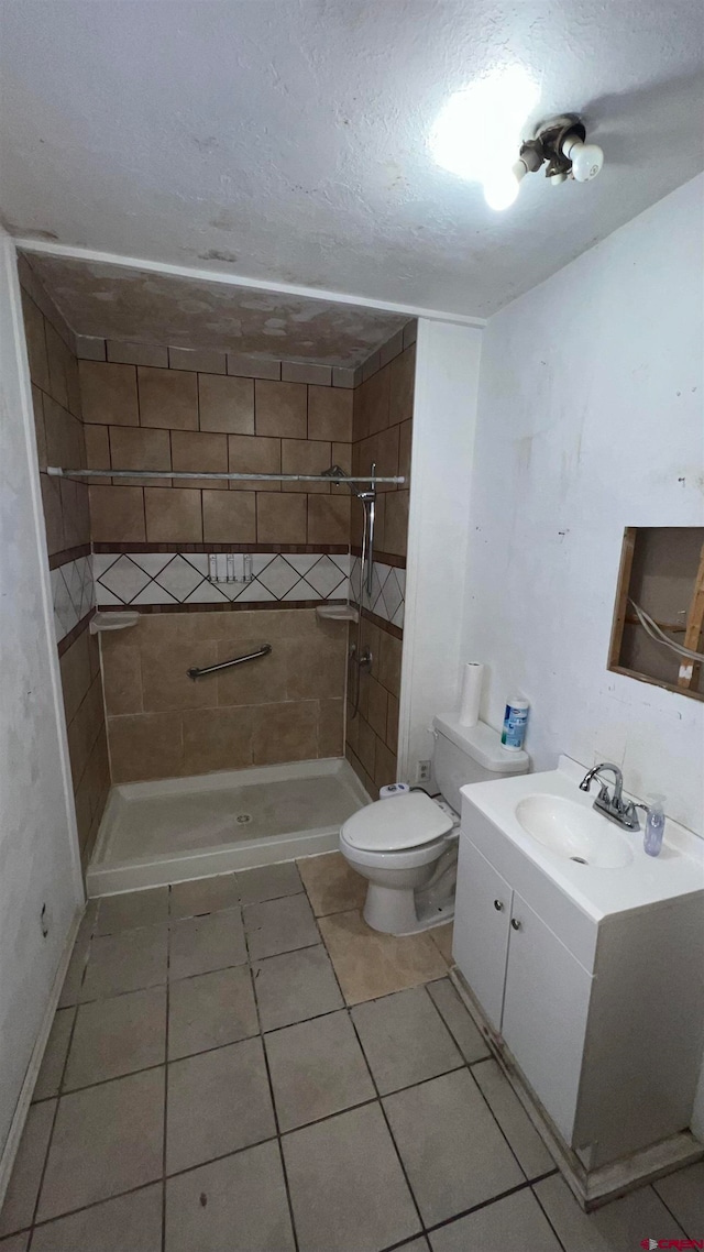 bathroom featuring tile patterned floors, a tile shower, vanity, a textured ceiling, and toilet