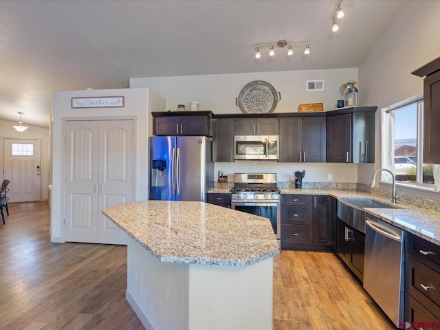 kitchen featuring a kitchen island, light stone countertops, stainless steel appliances, and light hardwood / wood-style flooring