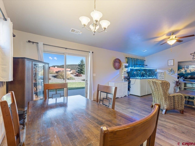 dining room featuring ceiling fan with notable chandelier, wood-type flooring, and vaulted ceiling