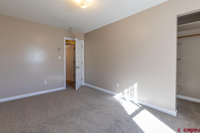 unfurnished bedroom featuring carpet flooring, a spacious closet, a textured ceiling, and a closet