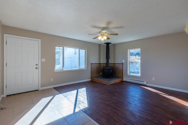 unfurnished living room featuring a textured ceiling, wood-type flooring, baseboard heating, and a wood stove