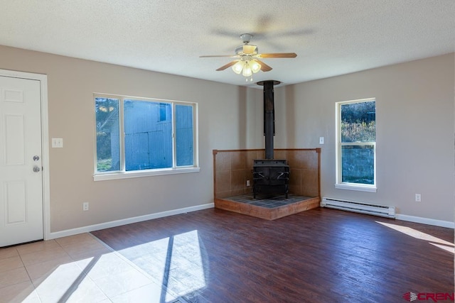 unfurnished living room featuring a wood stove, ceiling fan, a baseboard radiator, hardwood / wood-style floors, and a textured ceiling