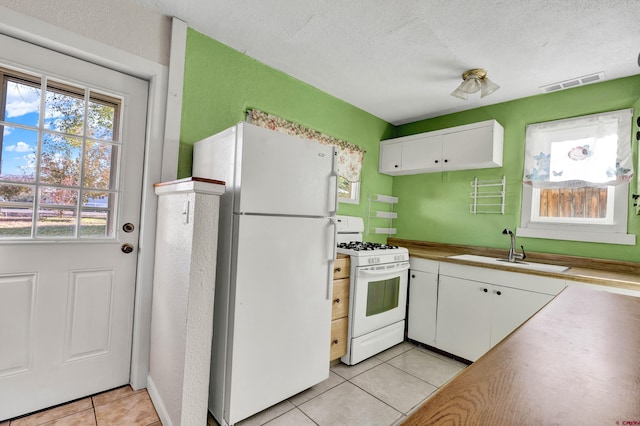 kitchen with white appliances, white cabinets, sink, light tile patterned floors, and a textured ceiling