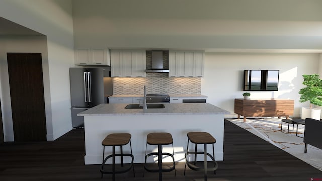 kitchen featuring wall chimney range hood, sink, stainless steel fridge, an island with sink, and tasteful backsplash