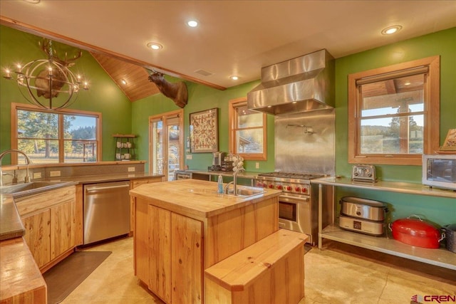 kitchen with wall chimney exhaust hood, stainless steel appliances, butcher block countertops, vaulted ceiling, and a center island with sink