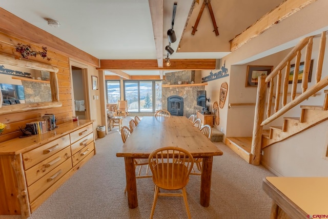 carpeted dining area featuring beam ceiling and a stone fireplace