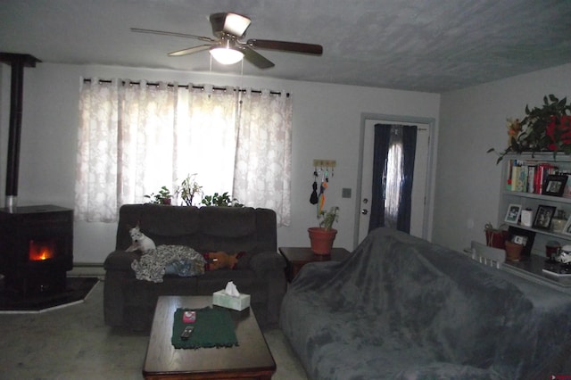 carpeted living room featuring baseboard heating, a wood stove, and ceiling fan