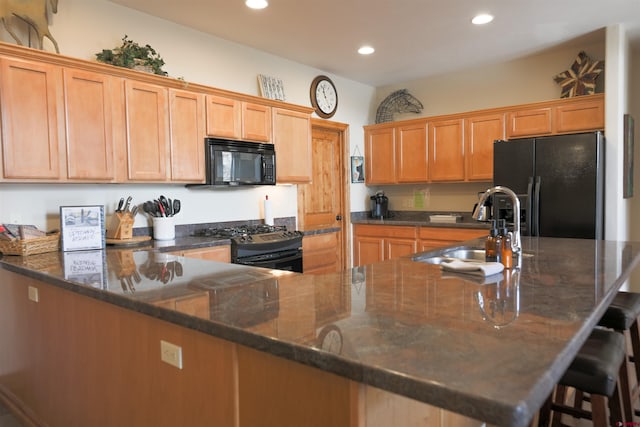 kitchen featuring dark stone countertops, black appliances, a breakfast bar area, and sink