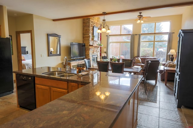 kitchen with a stone fireplace, black appliances, pendant lighting, sink, and ceiling fan with notable chandelier