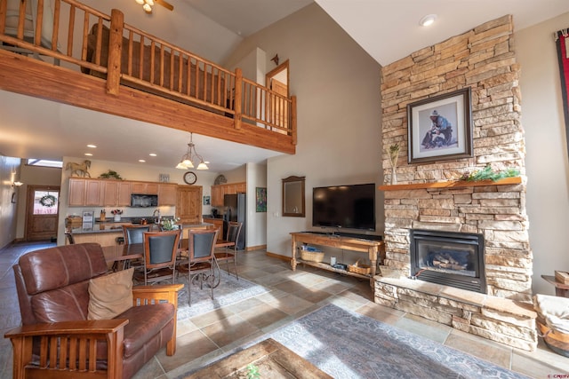 living room with high vaulted ceiling, a chandelier, and a stone fireplace