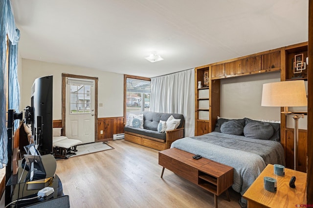 bedroom with light wood-type flooring, a baseboard heating unit, and wood walls