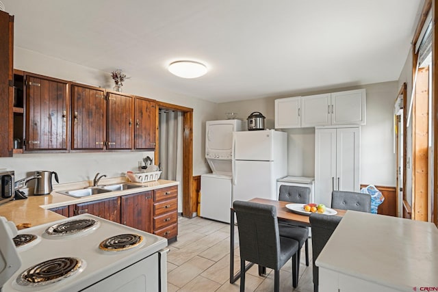 kitchen with white appliances, sink, dark brown cabinets, white cabinetry, and stacked washer / dryer