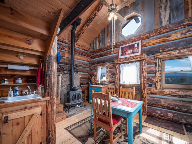 dining space with a wood stove, sink, high vaulted ceiling, beamed ceiling, and light wood-type flooring